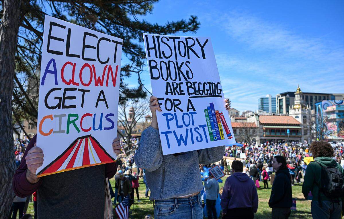 Protesters hold up signs at a No Kings rally against the Trump administration in Mill Creek Park near the Country Club Plaza on Saturday, March 28, 2026.
