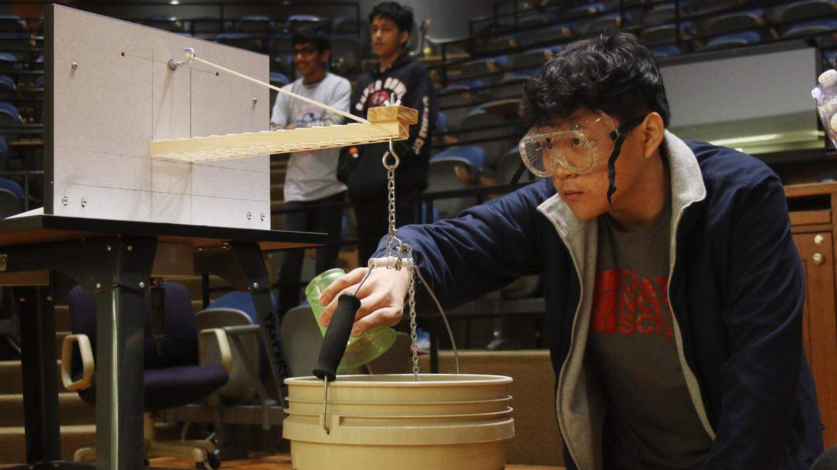 At the regional Science Olympiad competition Feb. 29, Olathe North senior Eddie Dai adds sand to a bucket to test how much weight his wooden structure can support.