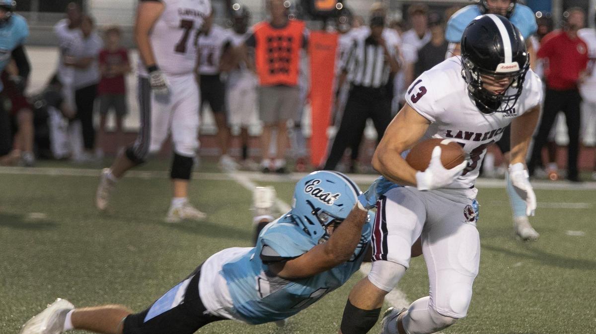 Ethan Curran (left) of Shawnee Mission East tries to stop Dominic Ostronic of Lawrence on a rushing play during Friday night’s game at the Shawnee Mission district stadium.
