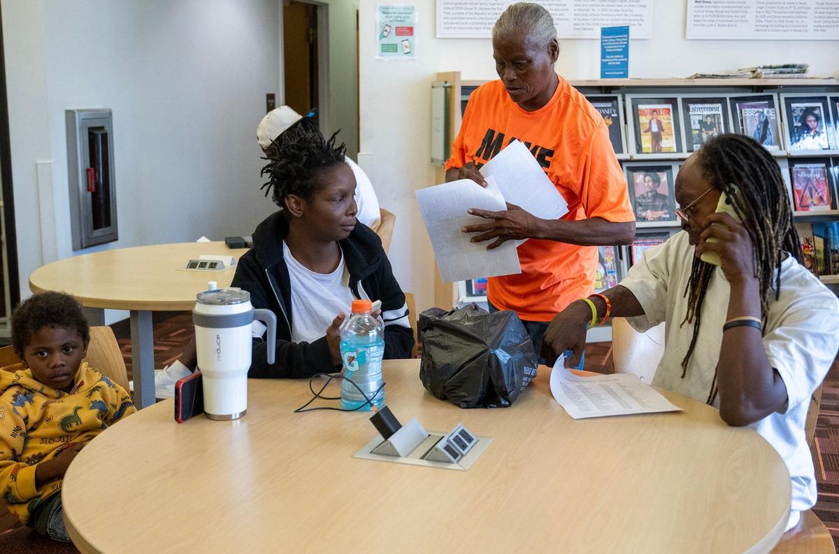 Vonzille Fayne, center, provides a Free Hot Soup meal location list to Deairra Wright, left, Ron Haynes, right, and their son, King James, 3, on Wednesday, Sept. 18, 2024, at Lucile H. Bluford Branch of the Kansas City Public LIbrary. The family was currently unhoused and visiting the library. Fayne, who was once unhoused, prints the lists for free at the library and supplies them to anyone who might need a free meal.