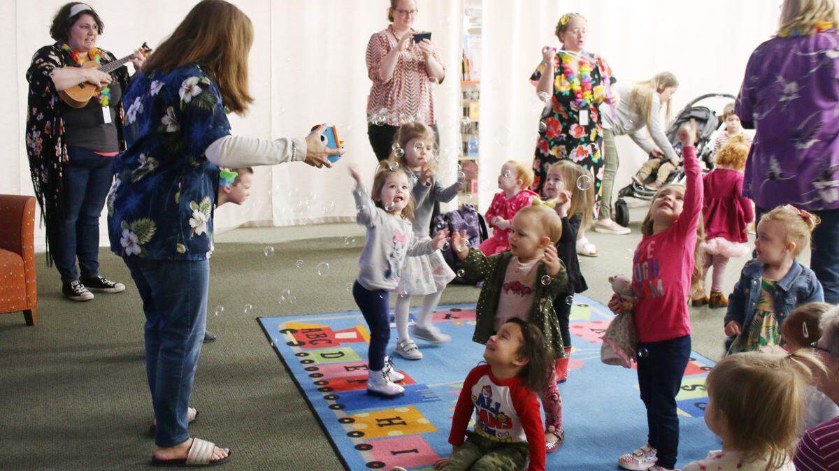 Early literacy associate Keri Wiester plays the ukelele as fellow early literacy associates Jill Fields and Sarah Richey send bubbles to float down over a group of children at the Colbern Road library’s winter luau program.