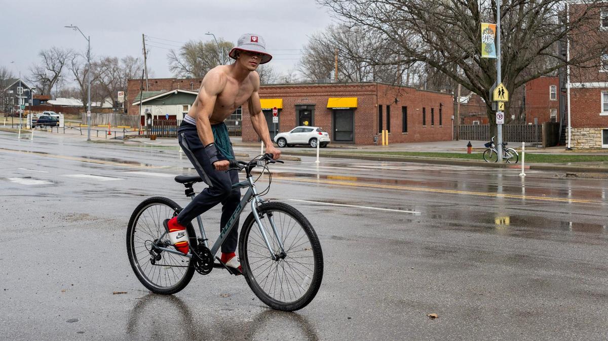 A shirtless cyclist rides down Gillham Road as rain begins to fall on Friday, March 14, 2025, in Kansas City.