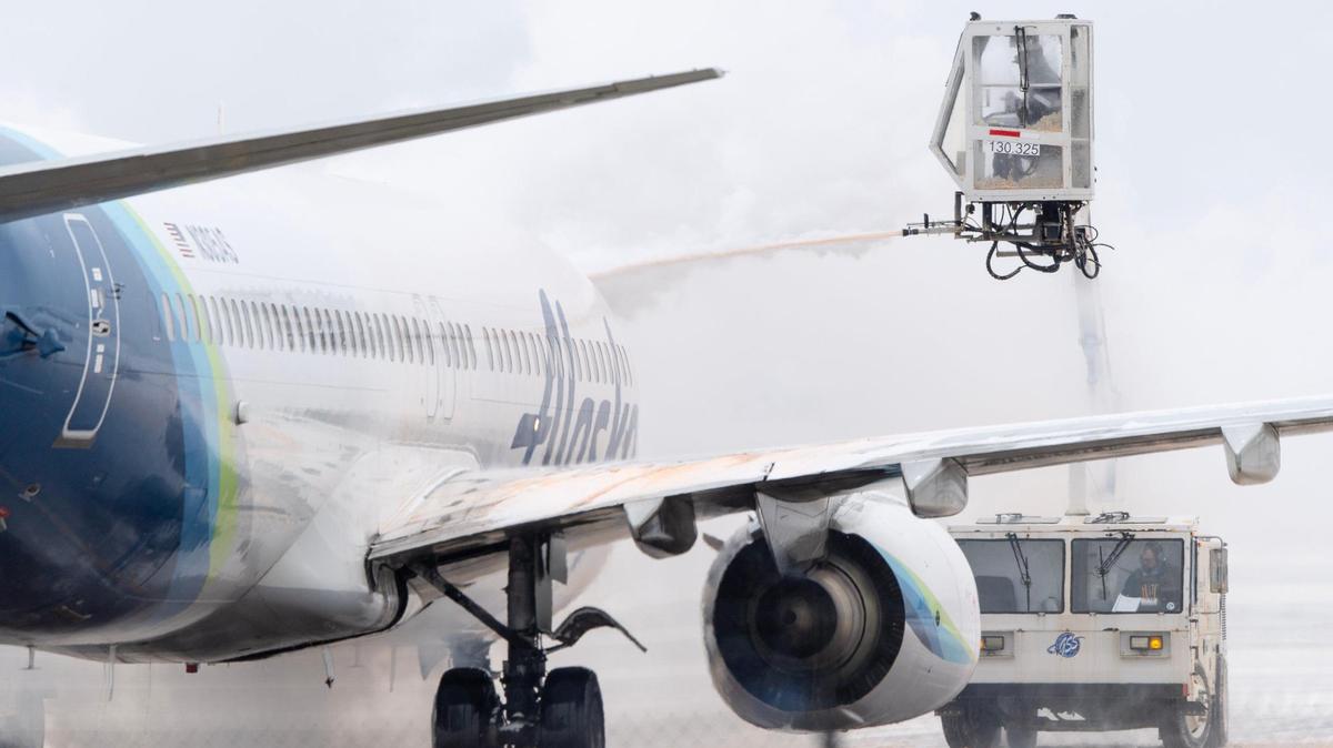 Holiday travelers with Southwest and Delta are facing a second day of flight cancellations and delays at Kansas City International Airport. A ground crew member deices an Alaska Airlines Boeing 737 passenger jet at the airport on Thursday.