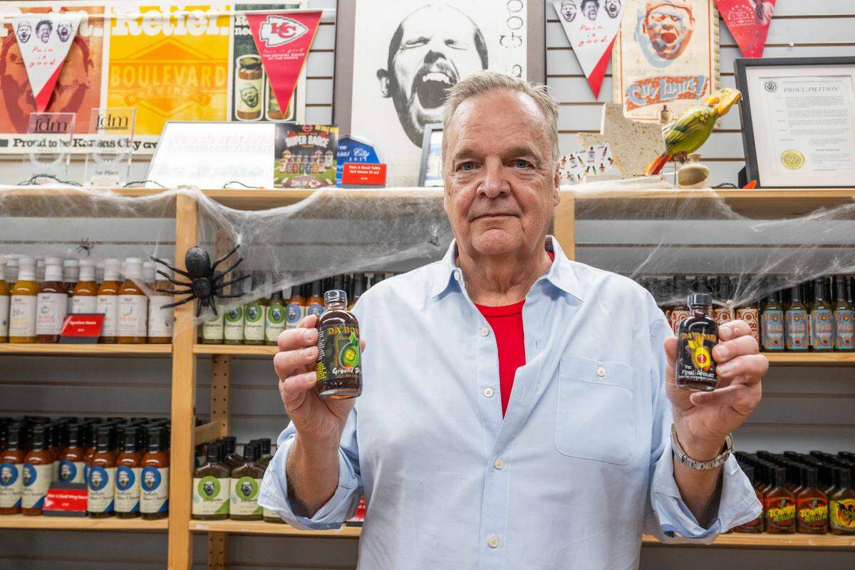 Scott Morse, owner of Spicin Foods, holds up two of the spiciest hot sauces in their hot sauce line-up, on October 2, 2025, at the Spicin Foods warehouse on Southwest Boulevard, in Kansas City. Morse said they didn't sell much of their most famous sauce, Da' Bomb Beyond Insanity, until the popularity boost of Hot Ones.