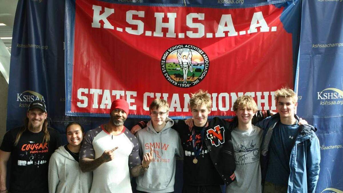 Will Ensley, 17, is pictured wearing a Shawnee Mission Northwest letterman jacket, alongside teammates and head swim coach Ryan Lee, at the 2023 Kansas State championships for swimming and diving.
