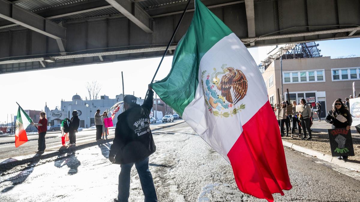 A man walks across the street waving a huge Mexican flag at a unity rally that drew scores of residents under the Interstate 35 bridge along Southwest Boulevard in Kansas City on Sunday.