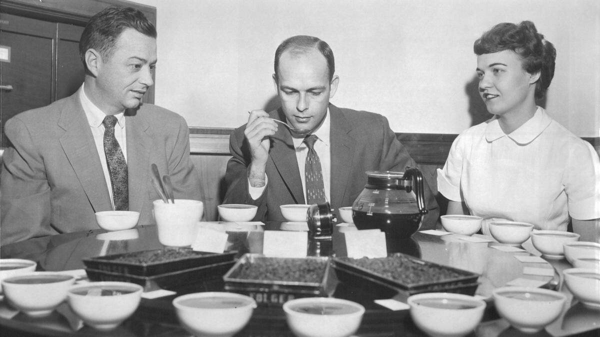 Gordon E. Atha, center and Vaughn L. Neblock, coffee testers at the Folger Coffee company in Kansas City, test samples from vari­ous plantation lots of coffee prepared by Folgers laboratory technician Ellen Lane in 1958.