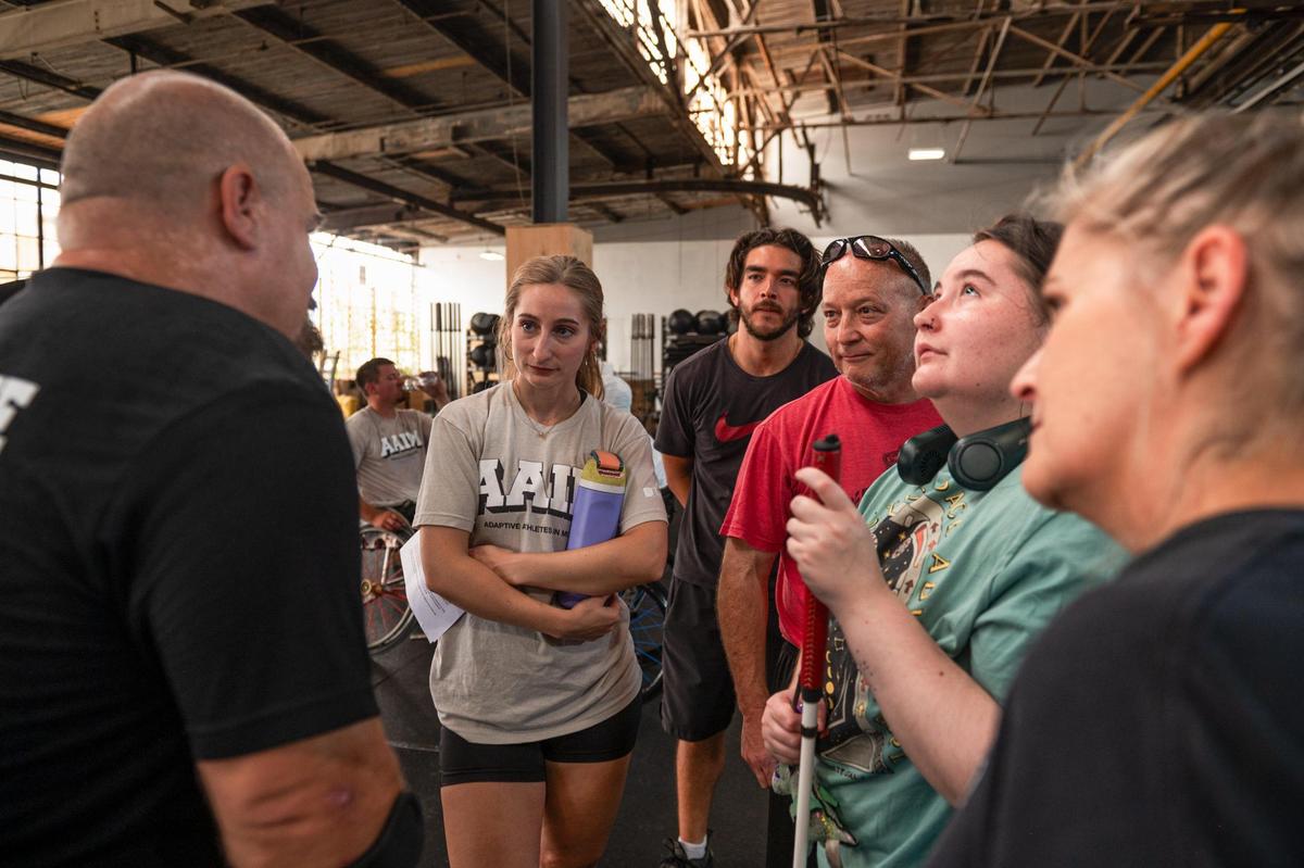 Adaptive Athletes in Motion coach Samantha Walker, left, and her family listen to Daniel Bufford speak at Brave Enough CrossFit. Walker joined as a coach with the AAIM program after her sister, Jordyn Walker, second from right, had an angioedema episode that left her sightless. Walker said she quit her job and followed her passion to help people who have disabilities like her sister.
