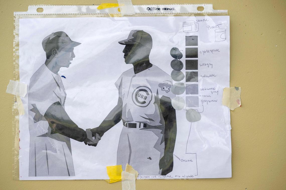 A color reference sheet is taped to a wall to guide artists painting the mural.