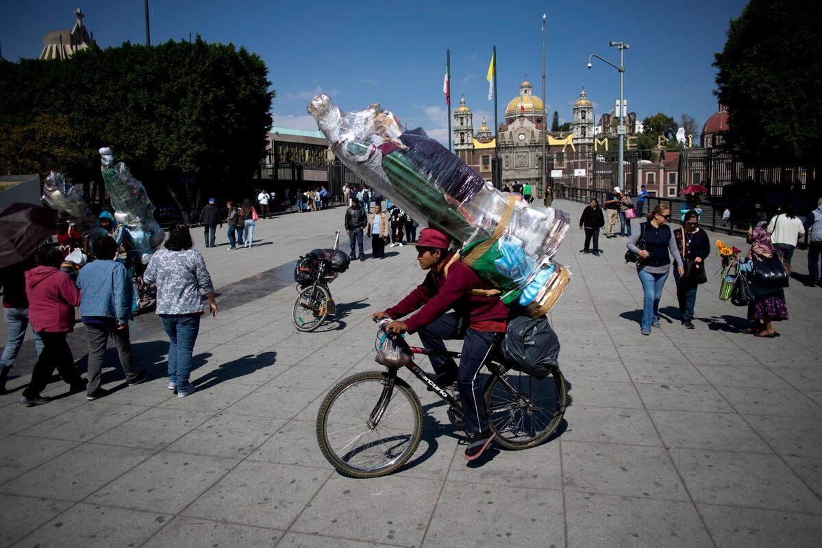 A cyclist carries two large statues of the Virgin Mary he bought from vendors outside the Basilica of Guadalupe, behind, in Mexico City, Wednesday, Nov. 22, 2017. The cyclist said he rode with a larger group to the capital from his state of Yucatan, starting on Nov. 5, as a pilgrimage to the Basilica in honor of Guadalupe. On Thursday, the group will return by bike and aim to arrive home just in time for her Dec. 12 feast day. (AP Photo/Eduardo Verdugo)