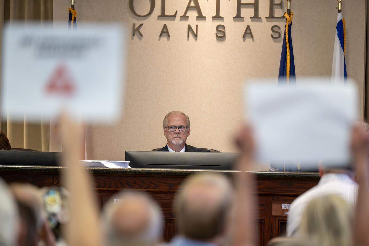 Olathe Mayor John Bacon watches as residents hold signs during the Olathe City Council meeting on Tuesday, Sept. 16, 2025, at Olathe City Hall. The council considered a proposed Lineage Cold Storage facility near 175th Street and Lone Elm Road.