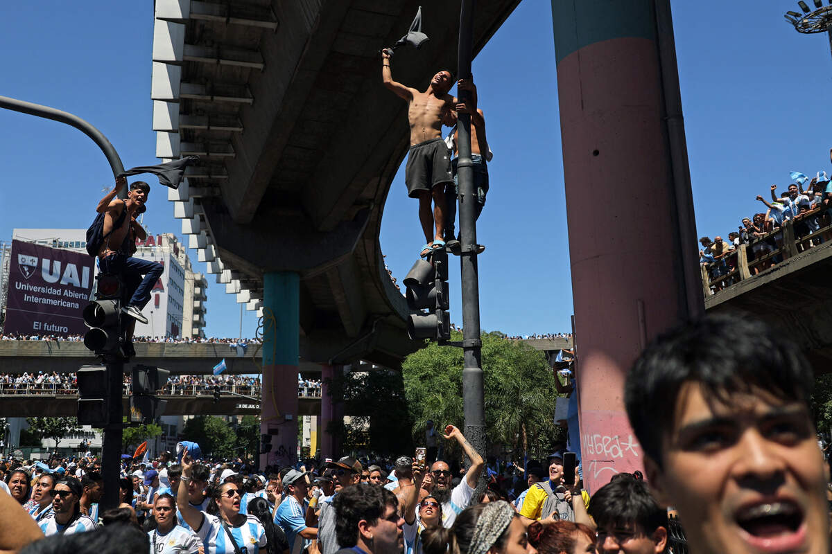 Fans of Argentina, some climbing street posts and beams, wait for the bus with Argentina’s players to pass through to celebrate after winning the Qatar 2022 World Cup tournament, in Buenos Aires on December 20, 2022.