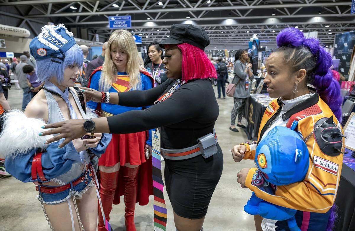 Diana Alexander, center, known to fans as "Diana the Great," inspects the intricate details of Thanh Tang's Rei Ayanami costume during festivities Sunday, March 29, 2026, at Planet Comicon Kansas City. Flanking the pair at Bartle Hall were fellow cosplayers Caroline Nelson of Just-us League in her Supergirl attire and Heather Geran dressed as Rumi of the Kpop Demon Hunters. In addition to cosplay, Alexander also designs costumes. 