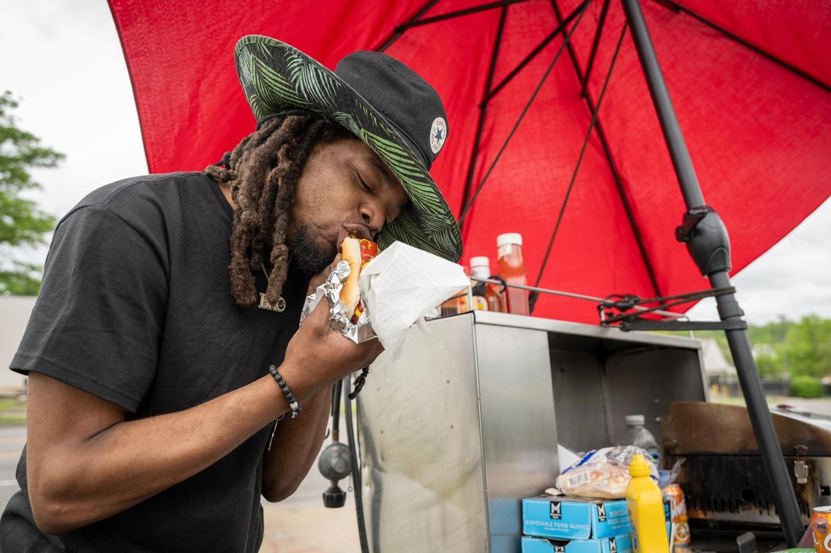 Robert Sims, an employee of a nearby auto supply store, bites into a hot dog he purchased from Jason Vanderlinden’s cart in the parking lot of From the Earth Dispensary, 6200 Troost Ave.