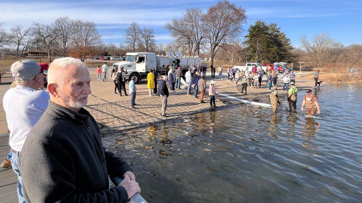 Jim Lancaster of Leawood, left foreground, was among the fishing enthusiasts who gathered to watch the first trout stocking of Shawnee Mission Lake in 2024. About 3,800 pounds of trout were deposited in the lake last week.