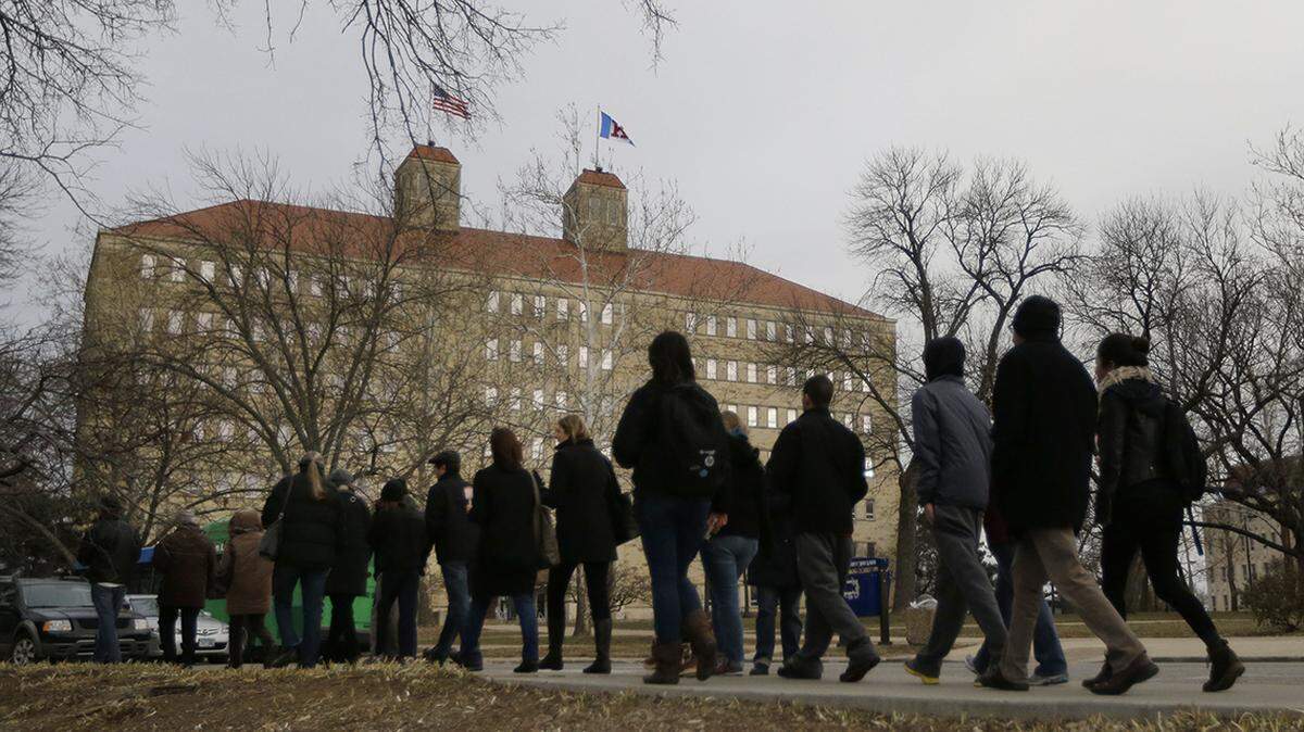 University of Kansas students and faculty walk past Fraser Hall on campus.