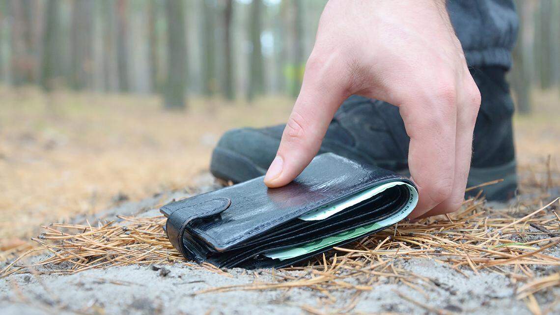 Male hand picking up lost wallet from a ground in autumn fir wood path. The concept of finding a valuable thing and good luck found find lose billfold