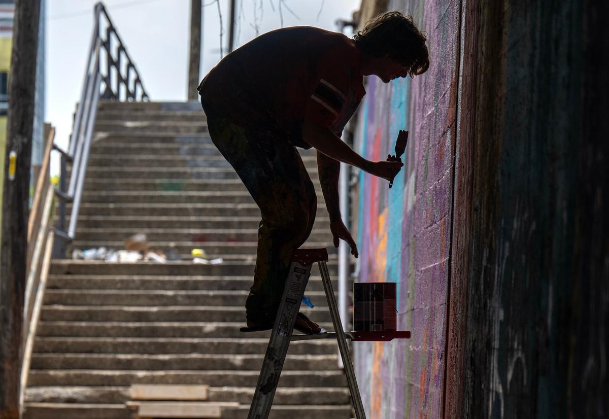 Artist Brian Mapes balances on a ladder while painting a mural at the Independence Ave. truck-eating bridge.