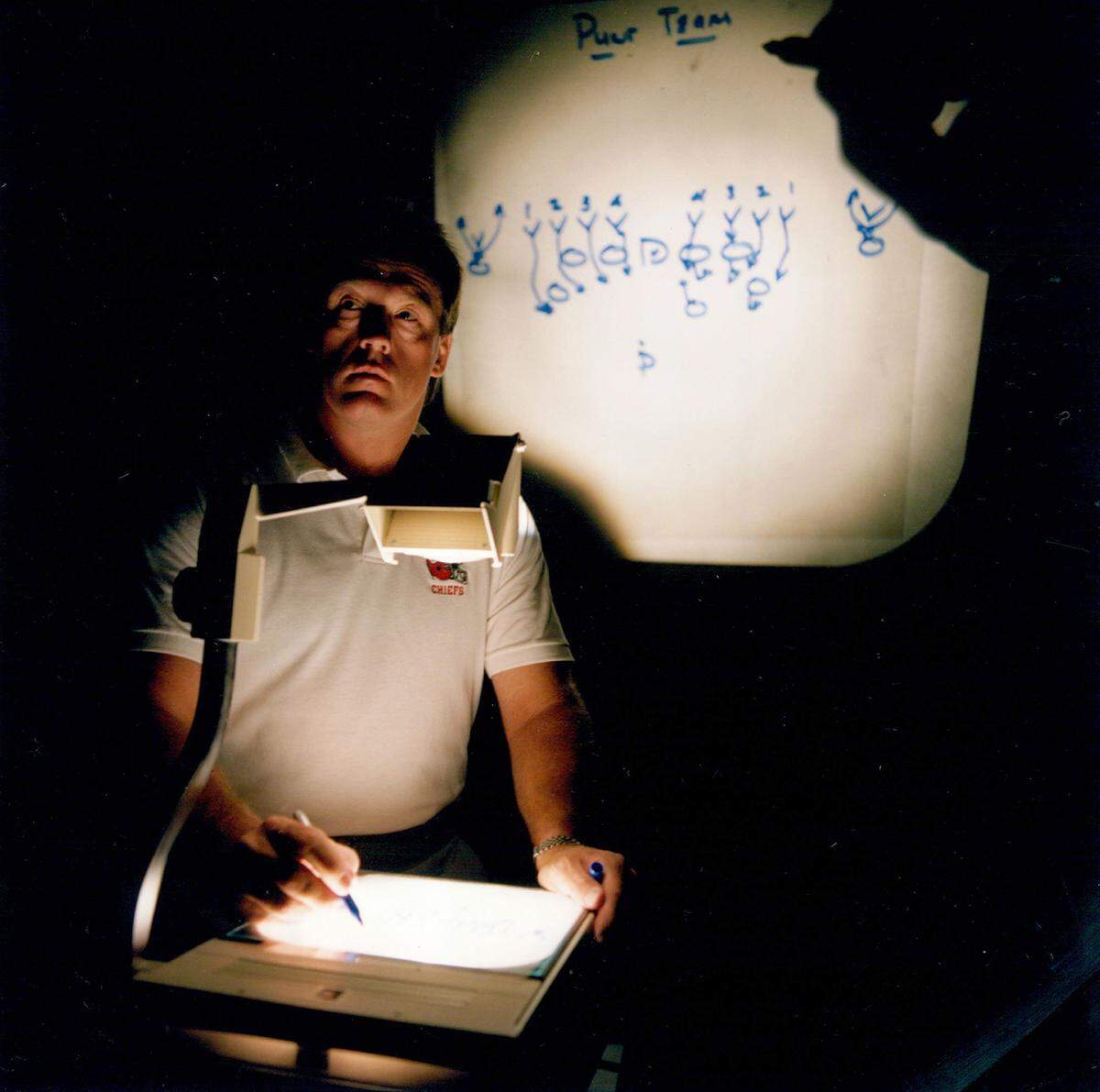 An overhead projector highlights special-teams coach Kurt Schottenheimer, brother of then head coach Marty Schottenheimer, as he demonstrates sometime in the 1990s how squiggles on the screen can become winning plays on the field. Classroom work takes up about 3 1/2 hours each day.