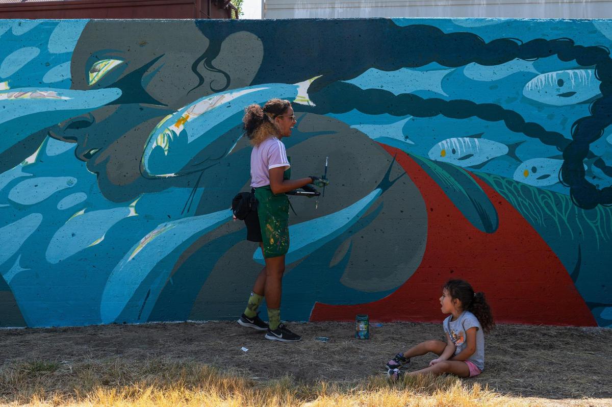 Emily Alvarez, left, laughs as Kira Wallace sits near by on Friday, Sept. 15, 2023, at the Riverfront Heritage Trial in Kansas City. Alvarez’s piece was inspired by fish in the Missouri River, her inclusion of a common bait fish found in the river is part of a larger commentary on harassment women face, she said.