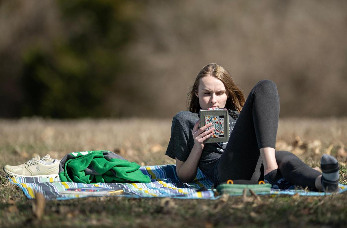 Taking advantage of the unseasonably warm weather, Jessika Henchek of Shawnee, relaxes on the hill and reads in a spot overlooking the lake at Shawnee Mission Park on Tuesday Feb. 27, 2024, in Shawnee, Kansas. Henchek, who works in a luxury pet hotel, says she always tries to get outside when the weather is nice.