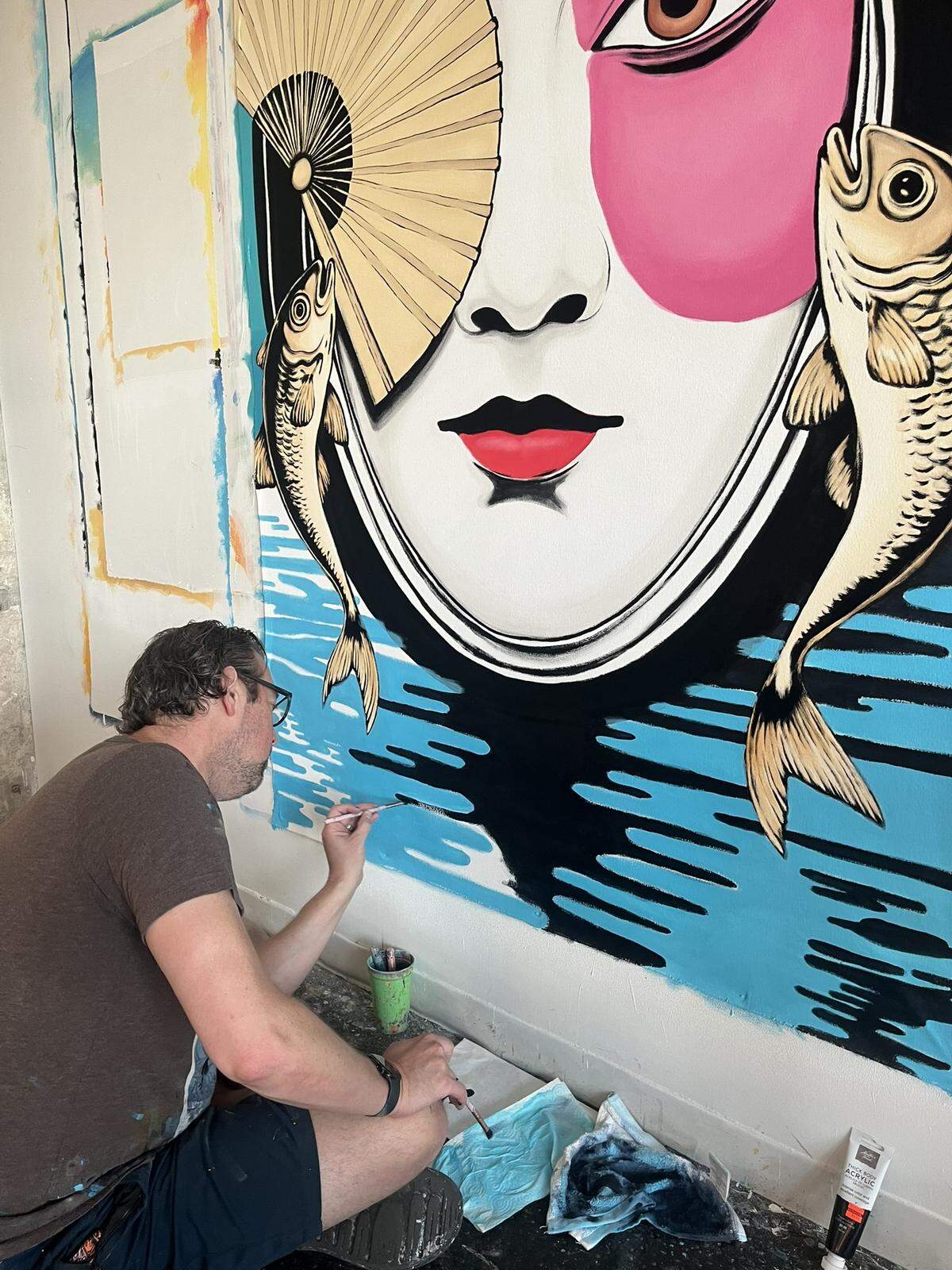 Overland Park artist Bryce Holt has completed 325 paintings, but has ideas for close to 250 more. He sits here painting a piece of a woman’s face with two fish placed on each side of her head.