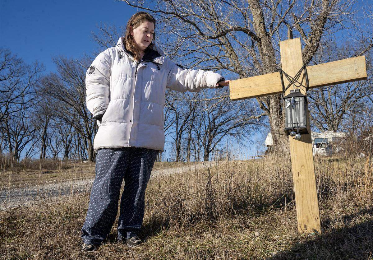 Ashlyn Clough, 35, who lives in the Holiday Lakes neighborhood, stands near a cross honoring the life of Airen Andula, 13, on Monday, Jan. 12, 2025, in Pleasanton in Linn County, Kansas. Airen, a beloved friend and neighbor, was found dead of multiple dog bites on Dec. 22, 2025, in a ditch in Bates County. Clough's husband and others built and erected the cross near an area where they believe Airen was attacked by dogs and killed. A solar lantern adorns the cross because Airen was afraid of the dark.
