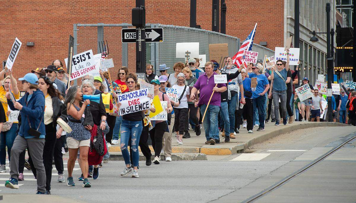 Demonstrators hold signs while they walk south along Main Street during a pro-democracy march that took aim at the Trump administration’s policies Saturday, March 29, 2025 in downtown Kansas City.