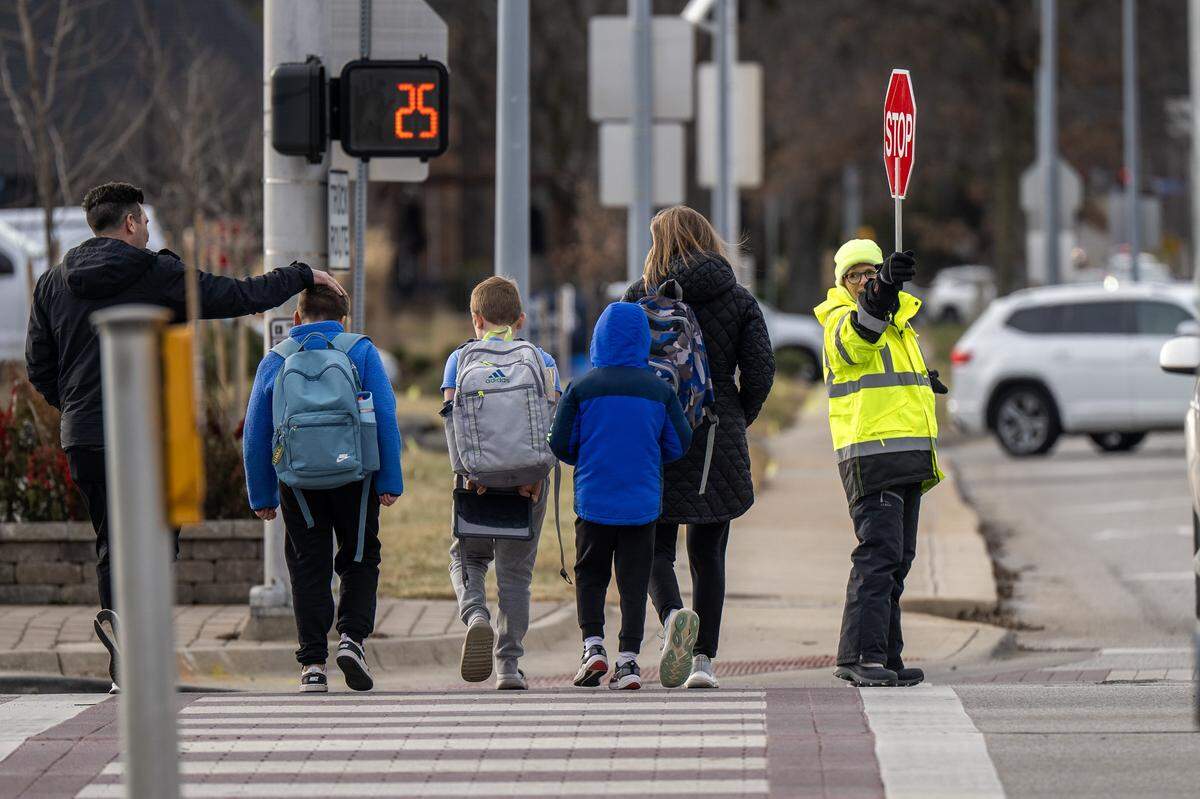 A crossing guard holds a stop sign as adults and children cross Mission Road near Corinth Elementary School on Thursday Jan. 15, 2026, in Leawood.