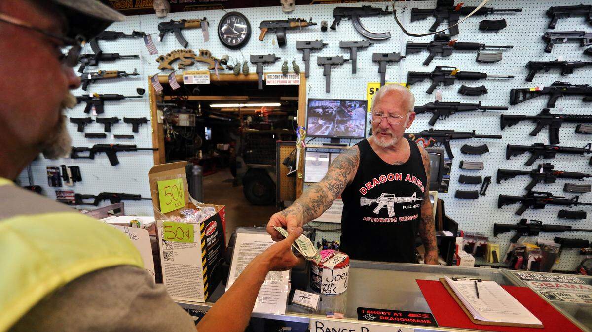 In this July 20, 2014 photo, with guns displayed for sale behind him, gun dealer Mel Bernstein gives a man his change while working the register at his store east of Colorado Springs, Colo. Bernstein has offered free AR-15 rifles to rabbis in the Colorado Springs area after the Pittsburgh synagogue massacre.
