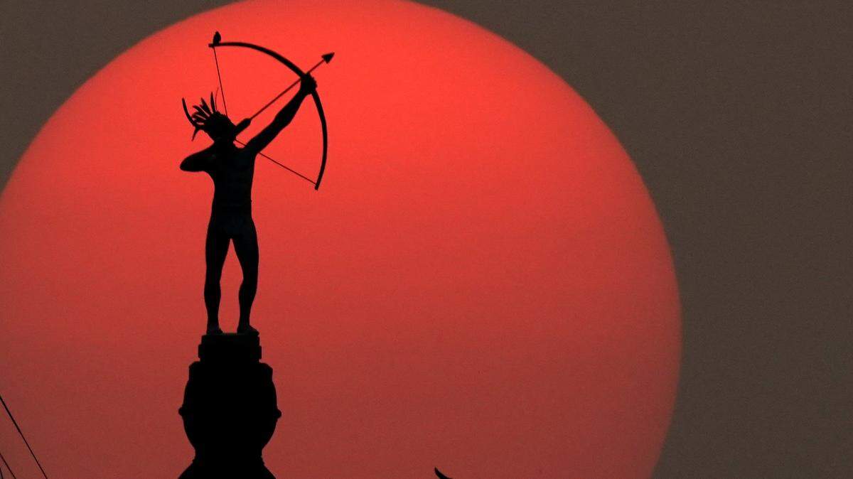 The bronze sculpture of Ad Astra, a Kansa Indian, perched atop the Kansas Statehouse dome, is silhouetted against the setting sun.