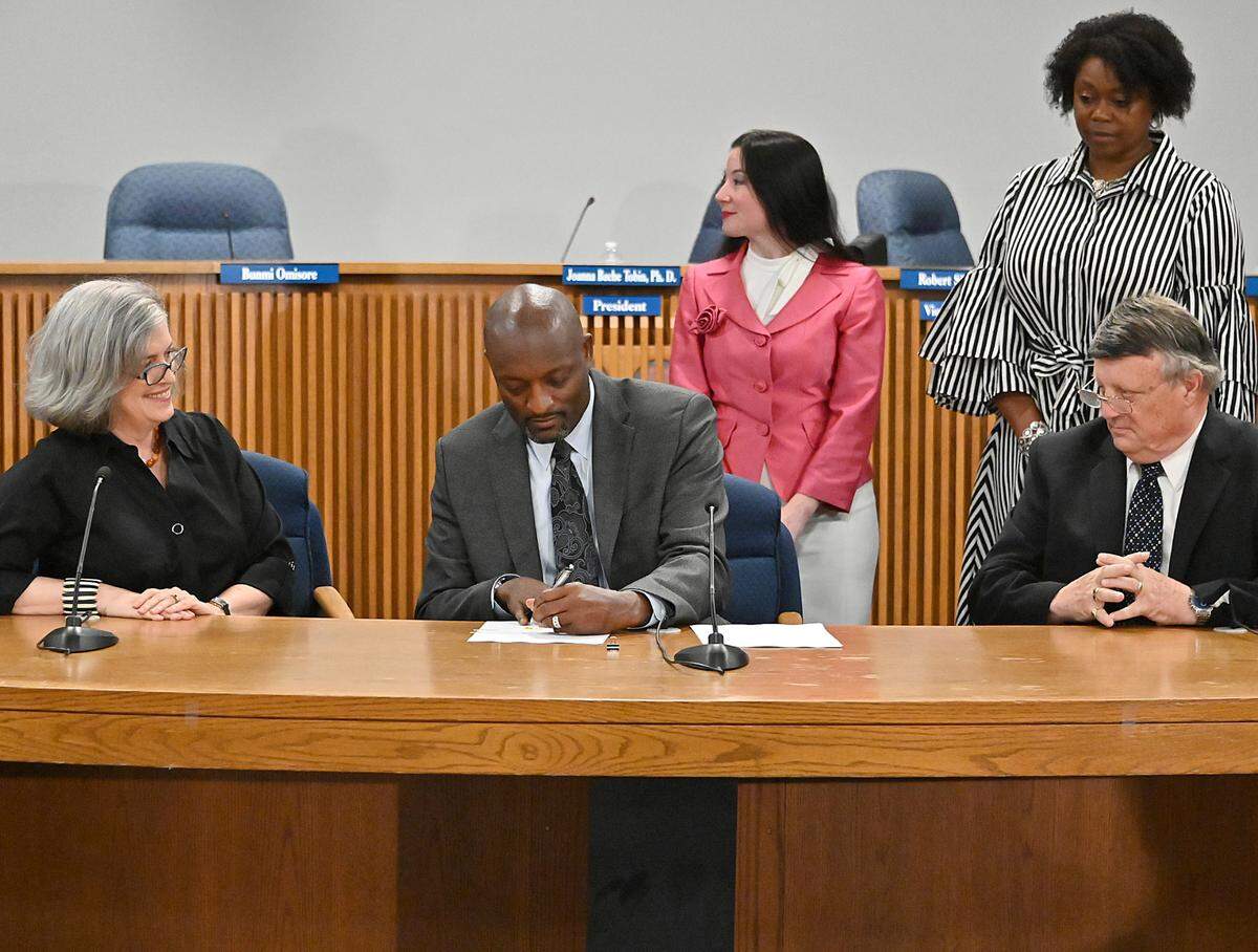 Mark Bedell signs his contract in the presence of the members of the board of education for the Anne Arundel County school district in Maryland, where he was introduced Friday as the next superintendent. Bedell is leaving Kansas City Public Schools in August.