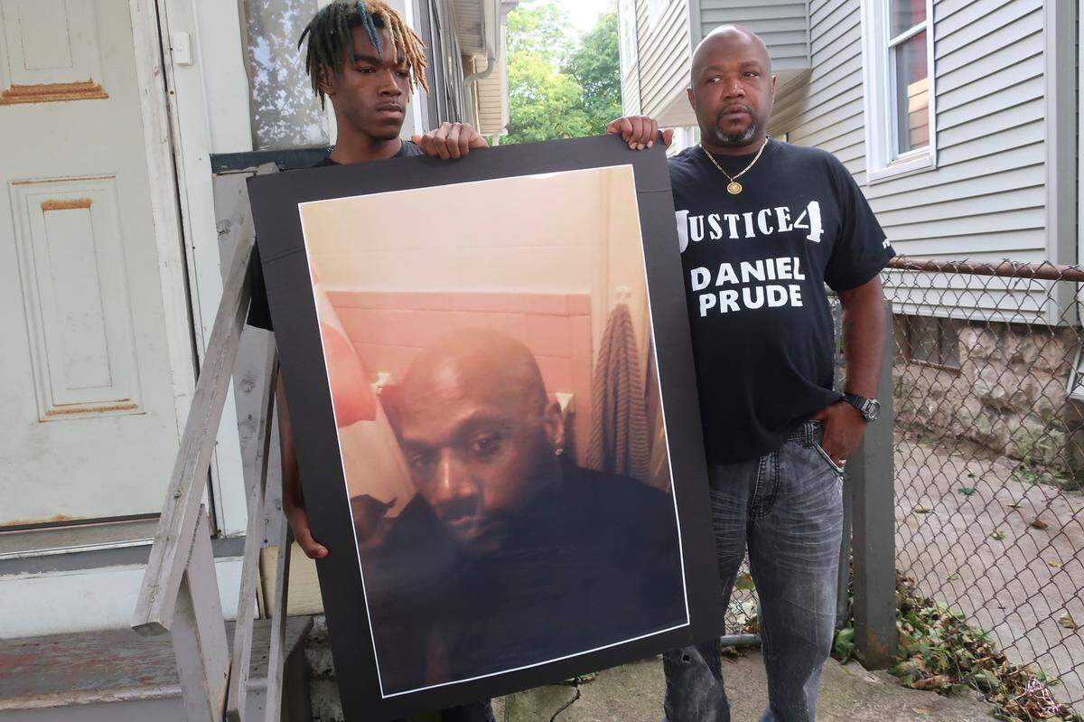 FILE - In this Sept. 3, 2020, file photo, Joe Prude, brother of Daniel Prude, right, and his son Armin, stand with a picture of Daniel Prude in Rochester, N.Y. Daniel Prude, 41, suffocated after police in Rochester put a “spit hood” over his head while he was being taken into custody. He died March 30, after he was taken off life support, seven days after the encounter with police. The independent investigator leading a probe of the city’s handling of Prude’s death says the ex-police chief is refusing to cooperate. (AP Photo/Ted Shaffre, File)