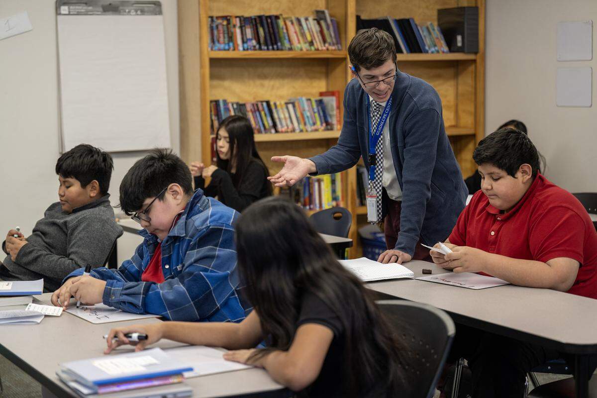 In his classroom, Christopher Leavens, an English language development teacher at Guadalupe Centers Middle School, talks to Jose, a seventh grade student, as he teaches a lesson on Thursday, Dec. 4, 2025, in Kansas City. The school does not have a library, so Leavens, has started a small library in his classroom so the students will have access to more books.