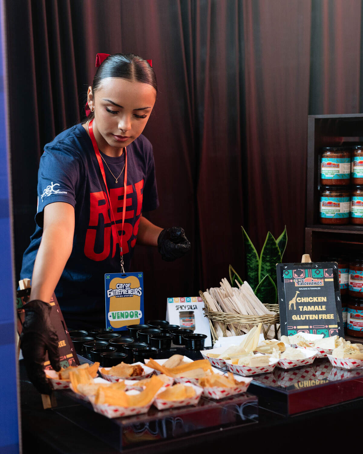 An attendant at Palomino’s Sauces and Tamales places sample-size salsa and tamales at City of Entrepreneurs Marketplace in union station on June 10, 2026. The woman and minority-owned business offers authentic Mexican flavors rooted in Kansas City culture.