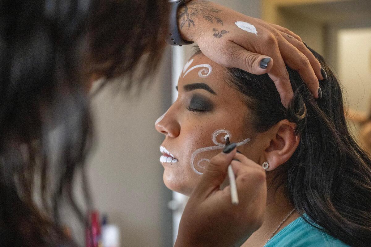 Zenaida Estrada sits patiently as she gets her face painted as a Catrina by Daniella Briones at Briones’ home before attending the Dia de los Muertos festival at the Mattie Rhodes Center on Friday, Nov. 3, 2023, in Kansas City.