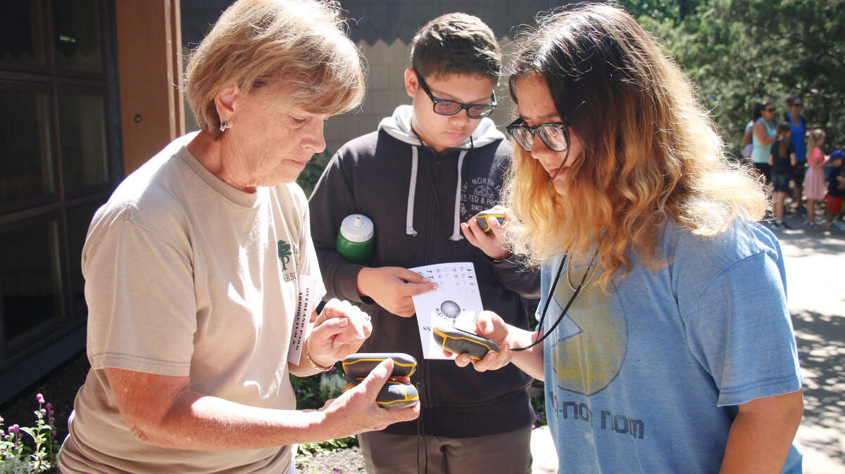 Volunteer Celeste Gogel helps William Snead and Aytumn Sanchez of Topeka get their GPS devices working during a GeoKids class at the arboretum.