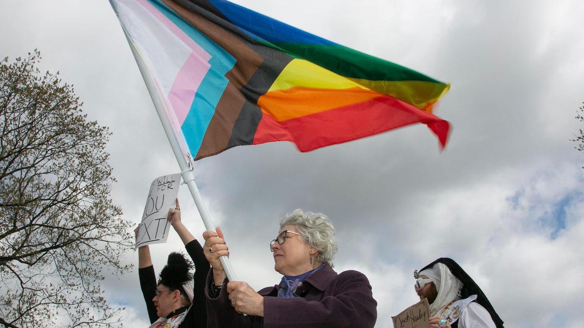 Marilee Harrison, with flag, and members of the City of Fountain Sisters, Novice Sister “Laffy Taffety” aka Robert Danley, left, and Sister “Dusty GustO’win” aka Gavin McReynolds joined transgender friends, family and communities Sunday, April 16 at Mill Creek Park on the plaza to protest Attorney General Andrew Bailey’s new executive action so strict that it will essentially ban gender-affirming care for many adults and minors in Missouri.