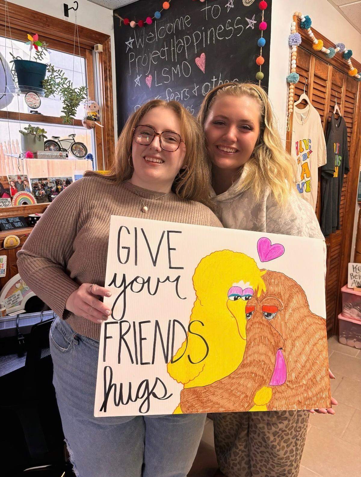 Georgia Hunsinger (left) serves as vice president of the nonprofit’s board, and Charlotte Hunsinger is among the volunteer sign makers for Project Happiness LSMO, founded by their mother Jennifer Hunsinger. Both sisters, who are holding a sign made by Georgia, make signs for the nonprofit.