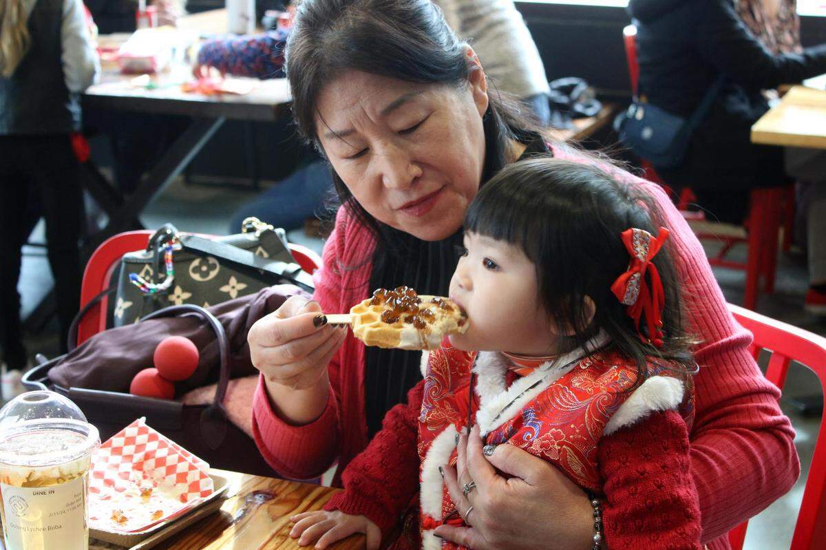 Overland Park resident Ming Ma helps her granddaughter, 18-month-old Kaitlin Ng, eat a brown sugar boba waffle at the Lenexa Public Market’s Lunar New Year celebration.