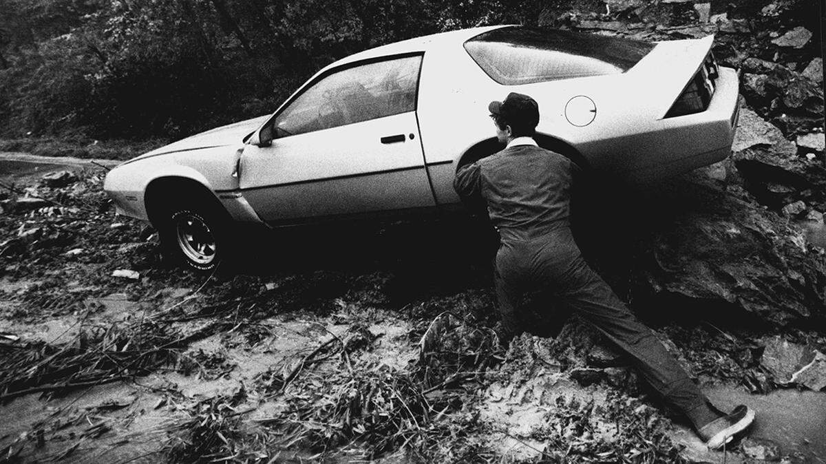 Heavy rain throughout Wednesday apparently weakened the east hillside on Beardsley Rd., just south of the 12th Street viaduct bringing this Camaro to a halt. Jim Darling, A Kansas City tow truck operator tries to attach a tow-chain before ruling the automobile free of the rock and mud. October 9, 1985