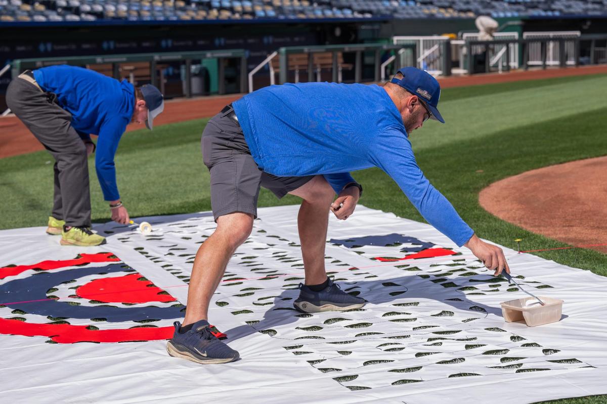 Grounds crew workers paint on a stencil for the MLB Opening Day logo to be painted on the field at Kauffman Stadium on Tuesday, March 25, 2025. Crews worked throughout the day to prepare for Opening Day for the Kansas City Royals.