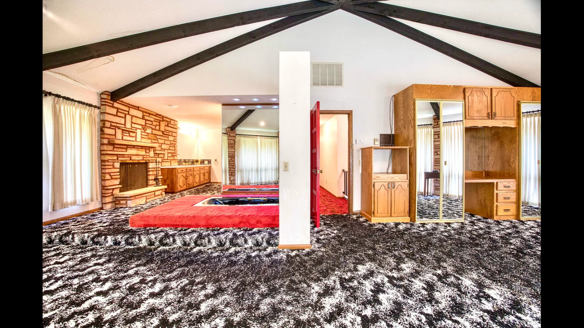 The master bedroom inside the home at 423 N. Belaire St. in Monett, Missouri .features a wall of windows and a sunken bath, all on carpet flooring.