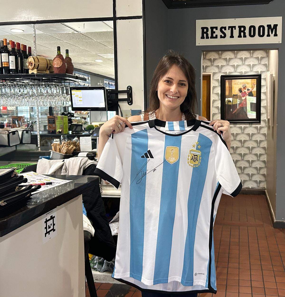 Isolina De La Vega, owner of Los Hornos, holds up her Lionel Messi jersey.