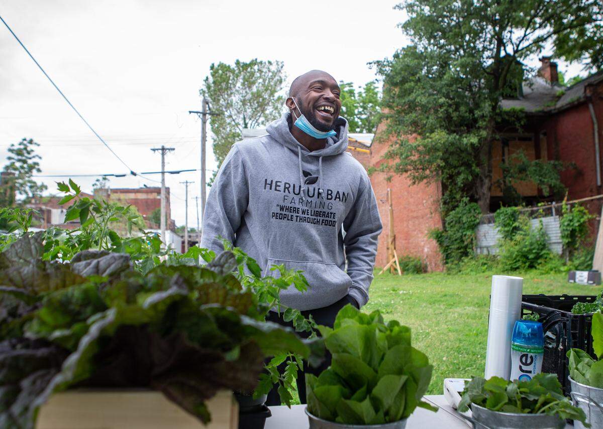 Tyrean Lewis, founder of Heru Urban Farming, laughs with customers at the Hyde Park Market in St. Louis. Lewis had spring greens and some pepper plants to sell at the market, all grown at his farm in Florissant, Missouri.