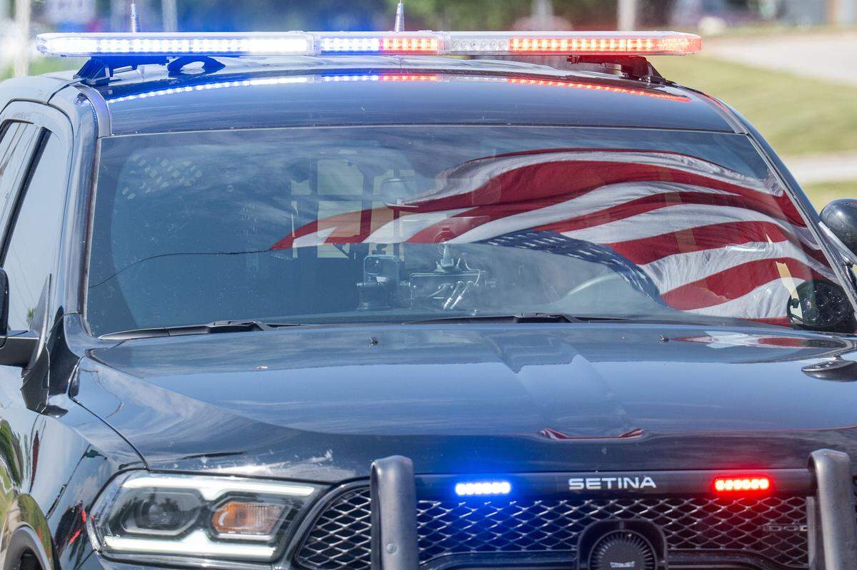 The American flag is reflected in the windshield of a police cruiser as police lead a funeral processional for slain KCKPD Officer Hunter Simoncic, on Wednesday, Sept. 3, 2025, in Kansas City, Kansas. Simoncic was killed Aug. 26 after being struck by a fleeing driver while deploying stop sticks.
