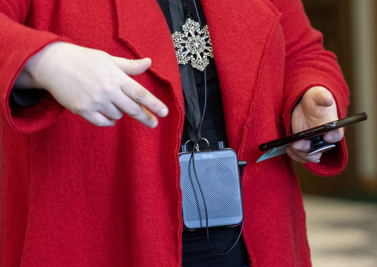 Wearing a speaker around her neck, music teacher Rachel Marlow played songs from her phone and directed the special chorus from Central Elementary as they sang holiday carols at businesses in downtown Olathe on Wednesday, Dec. 17, 2025.
