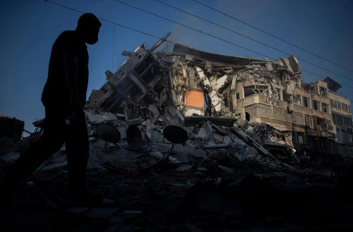 Palestinians walk next to the remains of a destroyed 15 story building after being hit by Israeli airstrikes on Gaza City, Thursday, May 13, 2021.