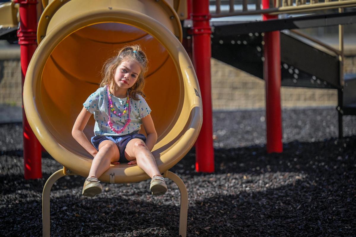 Hattie Foster, 6, sits on the slide at Prairie Elementary School on Sunday, April 2, 2023, in Prairie Village. Hattie’s parents, Michael and Melissa Foster of MIssion Hills, take Hattie, who has SYNGAP1, a neurological disorder, which causes intellectual disabilities, gastro issues, autism, sleep issues, aggression, gait issues and epilepsy, to the playground during off-hours because she can be aggressive toward other children. Despite her two brothers being at the playground, Hattie mostly played by herself.
