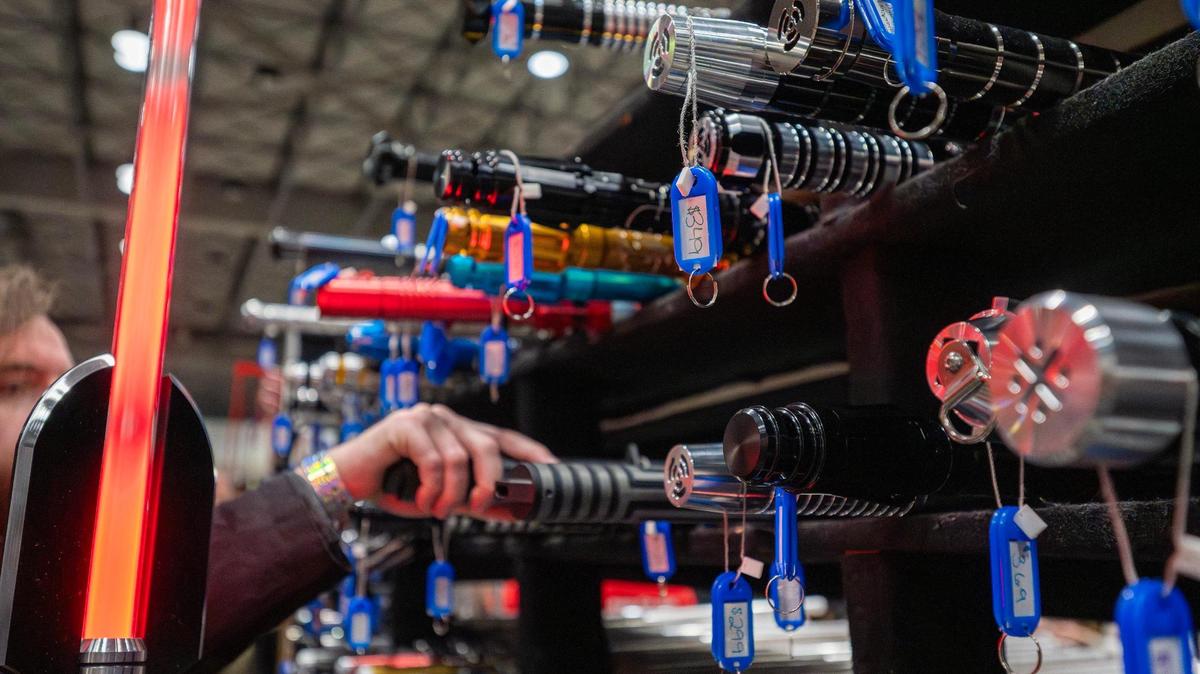 Visitors browse lightsabers displayed in cubby-like shelves, including one priced at $349, during Planet Comicon at the Kansas City Convention Center on Saturday, March 22, 2025.